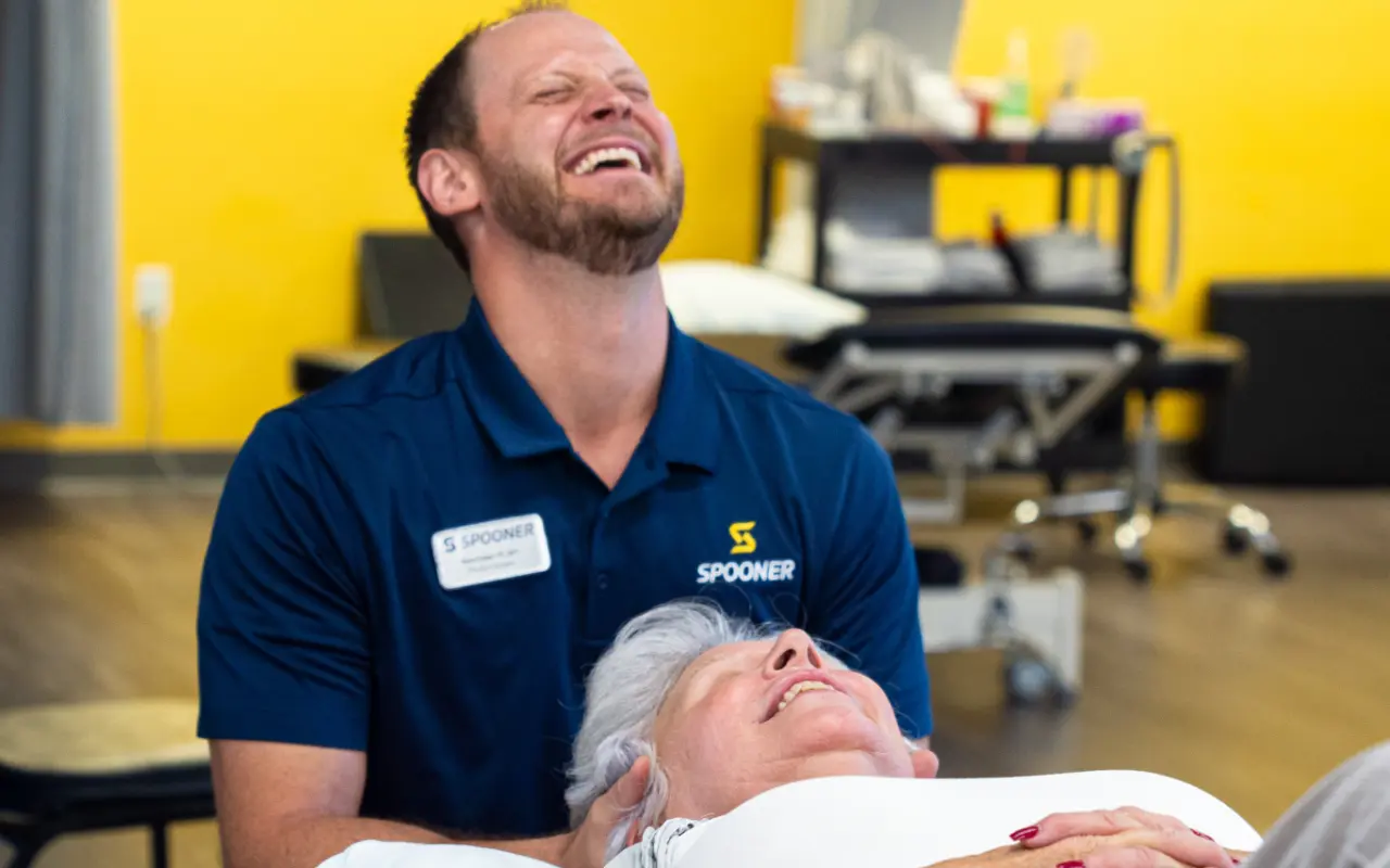 A therapist laughing while doing a neck adjustment on a patient.