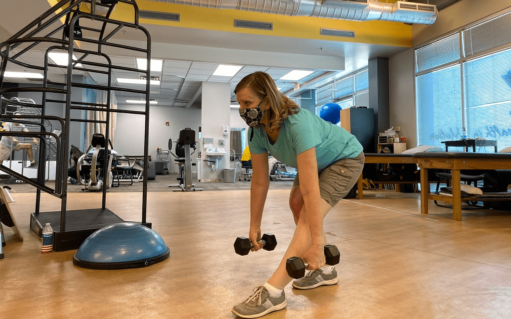 A woman holding dumbbells and leaning forward.