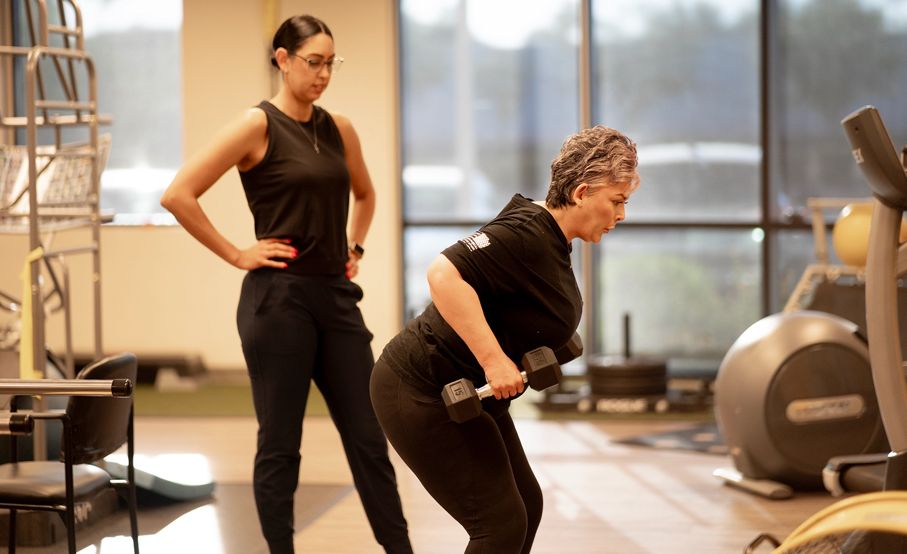 A breast cancer survivor doing bent over rows with dumbbells as Andrea Renteria, PT, DPT monitors her form.