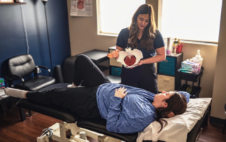 A pelvic health therapist showing a pelvic floor model to a patient as the patient lays on a table.