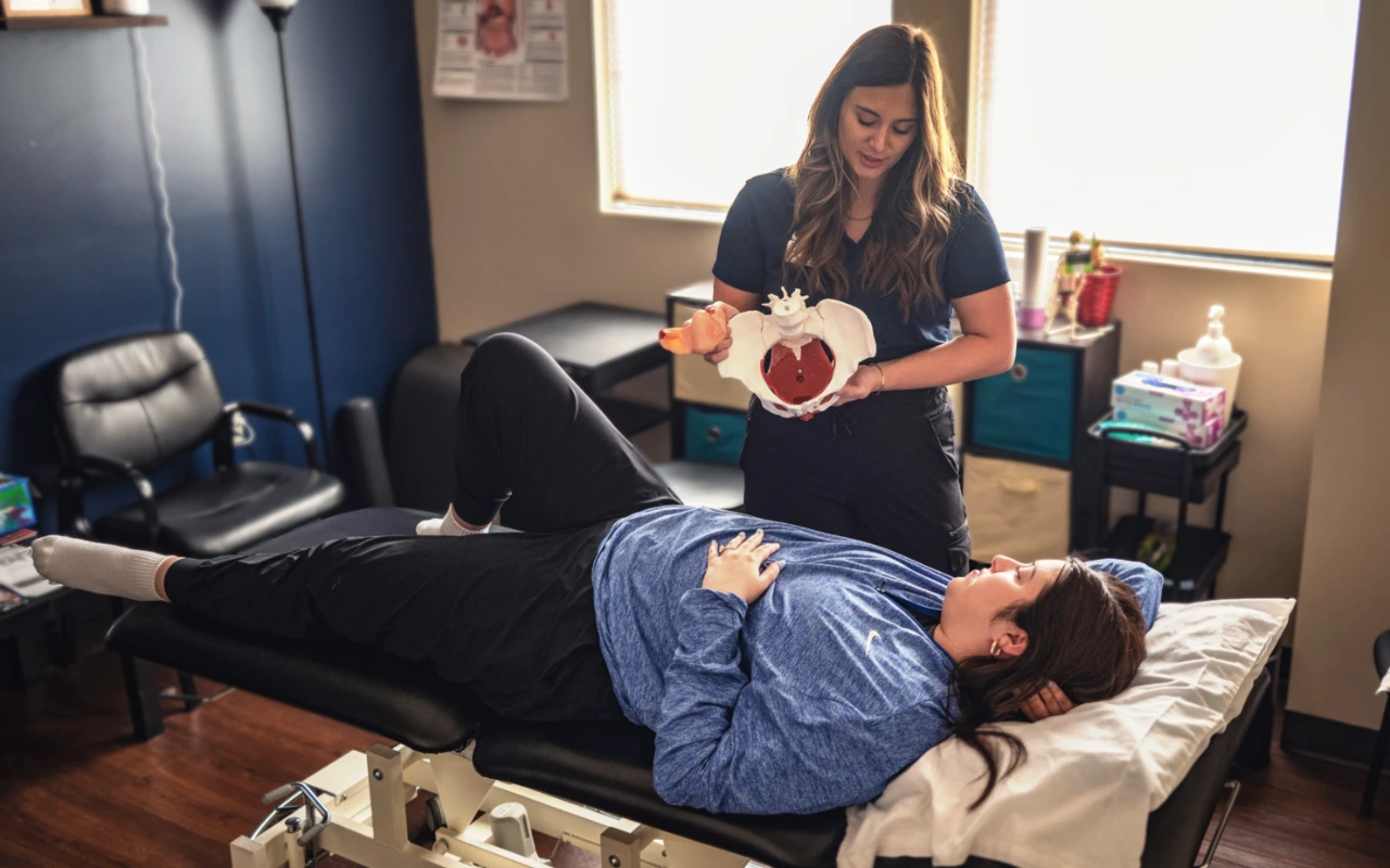 A pelvic health therapist showing a pelvic floor model to a patient as the patient lays on a table.
