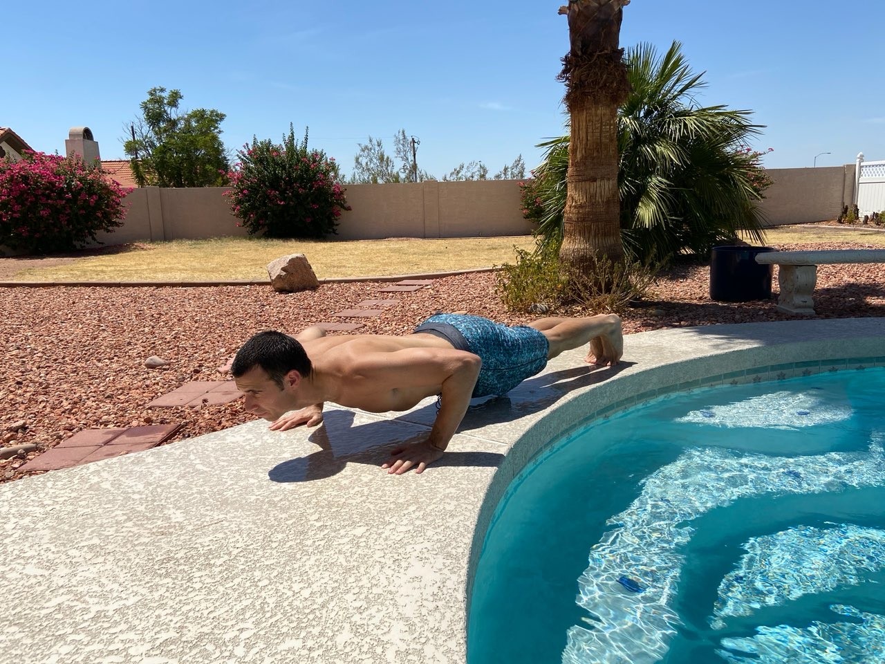 a man doing a pushup next to a pool.