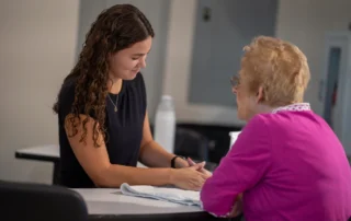 A hand therapist working with an older woman in a pink shirt.