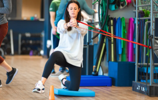A woman kneeling on a blue pad as she lifts her leg over a cone.