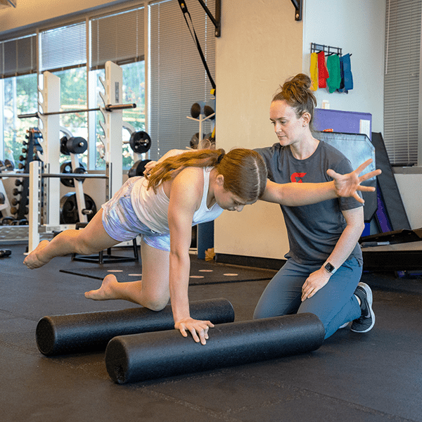 Alyssya holding the back of a gymnast as the gymnast practices superman exercises as she balances on 2 foam rollers