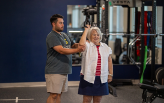 A physical therapist helping an older woman lift a kettlebell over her head