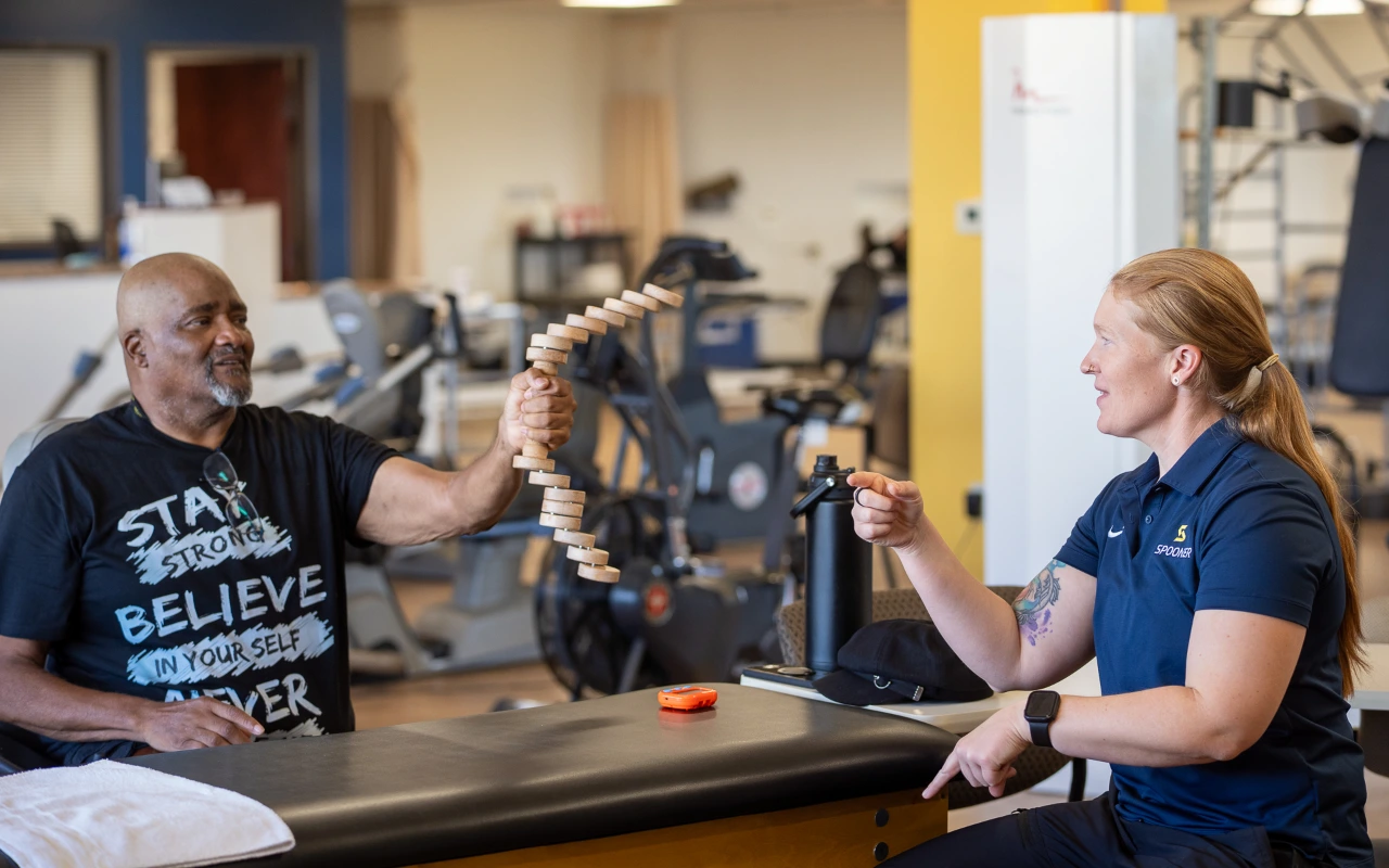 Tara Wright, OTR/L, CHT giving a man instruction on what to do with the tool he is holding for his hand exercises.