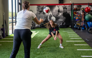 A volleyball player hits a ball back to a physical therapist.