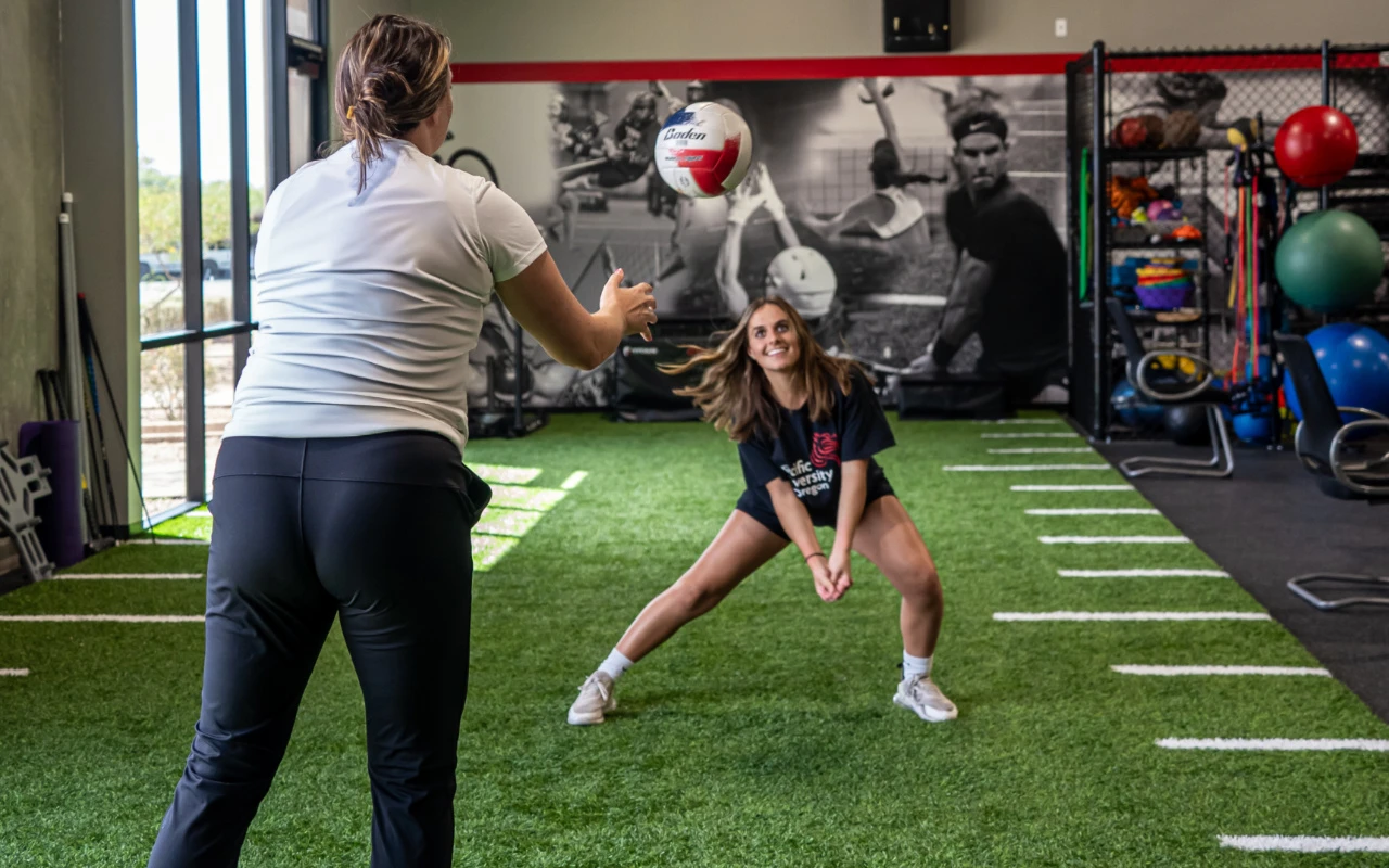 A volleyball player hits a ball back to a physical therapist.
