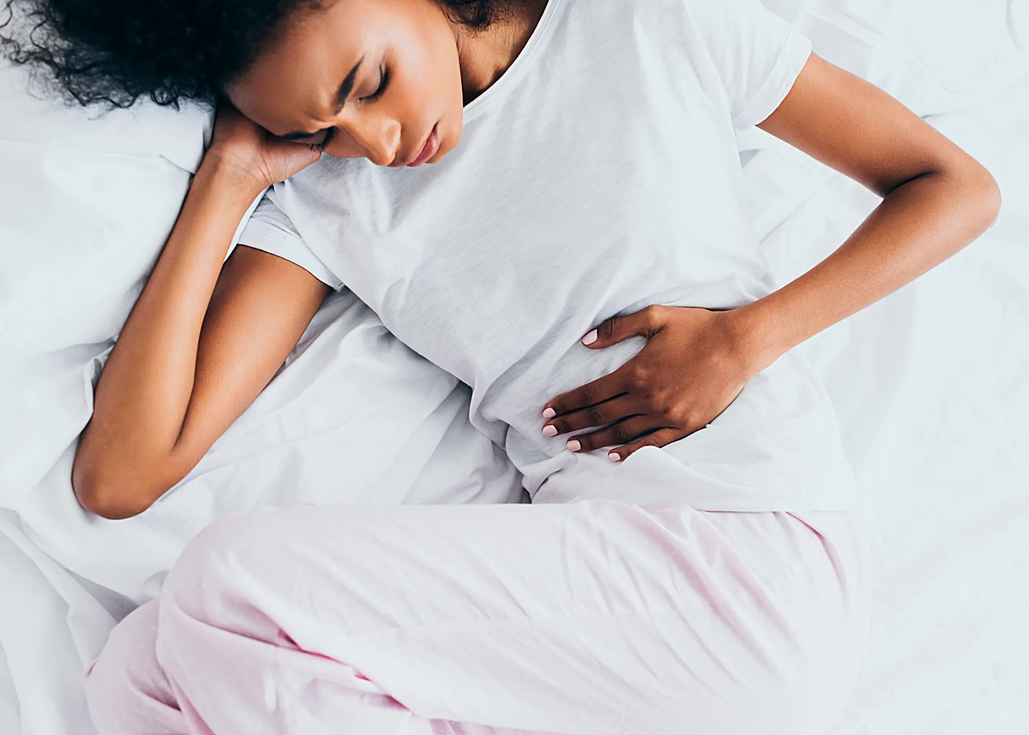 Woman laying on a bed holding her stomach.