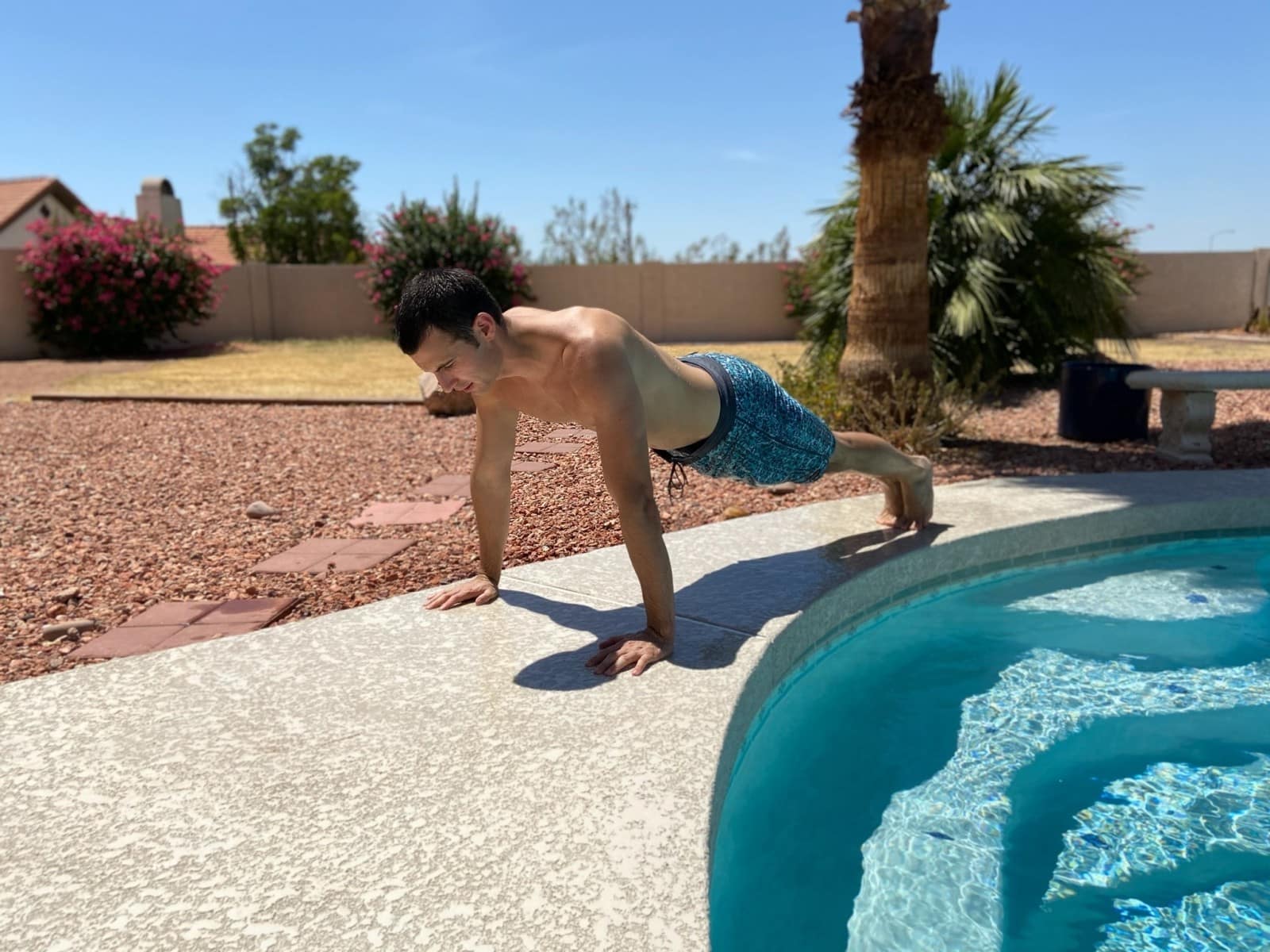 A man doing a pushup next to a pool.