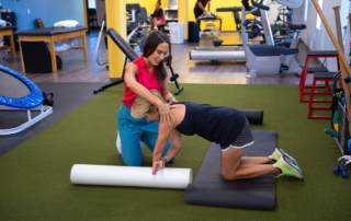 Feature image of a therapist holding the shoulders of a patient as she uses a foam roller.