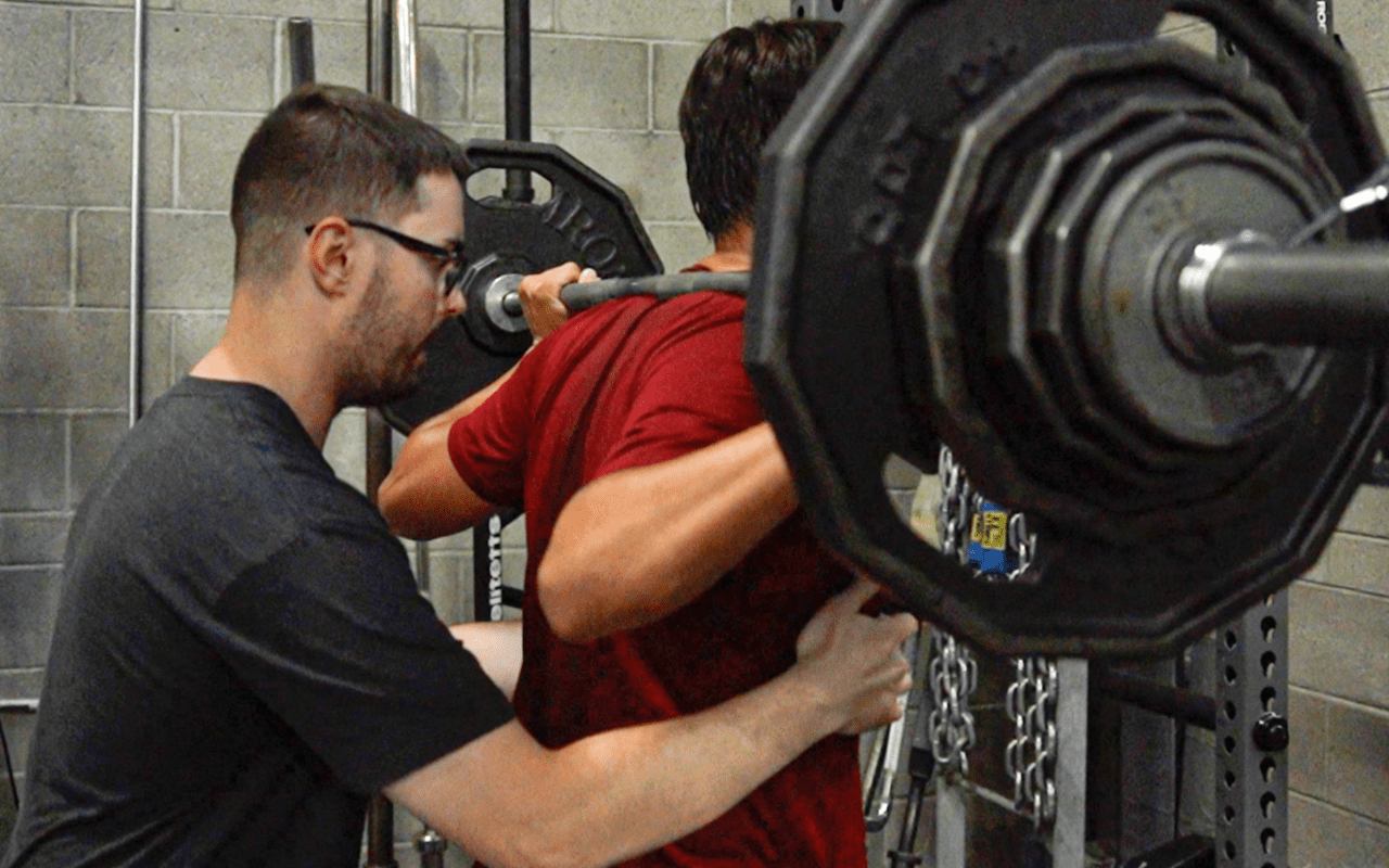 A FIT Trainer helping a patient perform barbell squat.