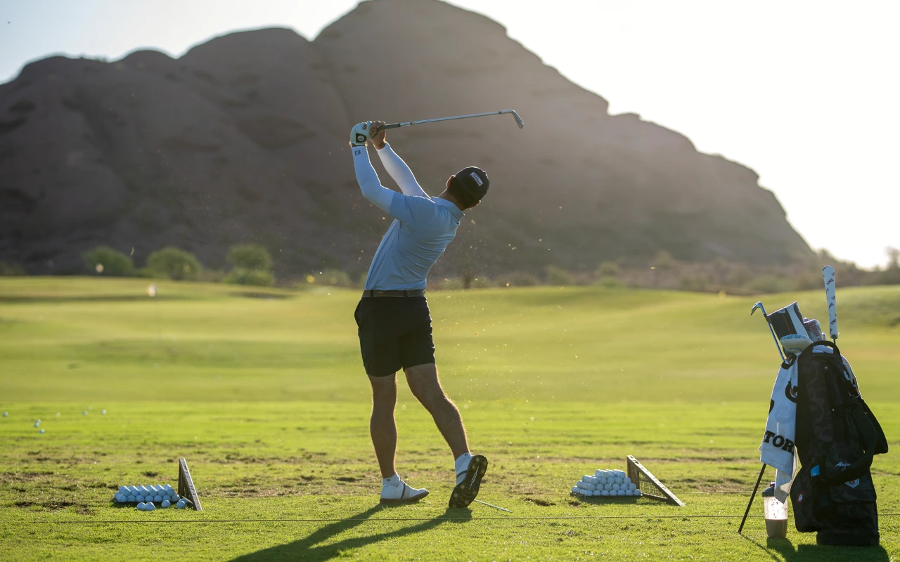 A golfer swinging on the turf towards a mountain.