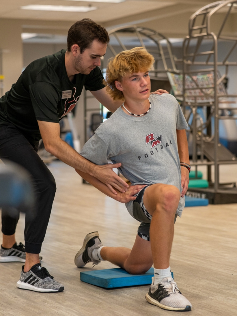 Male teen athlete kneeling on a blue pad demonstrating the sagittal plane of motion by leaning to the side.