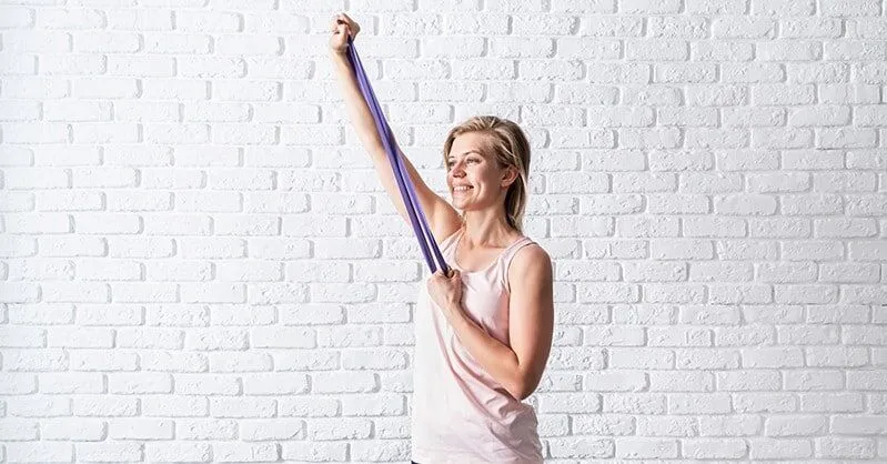 A woman stretching at home against a white wall.
