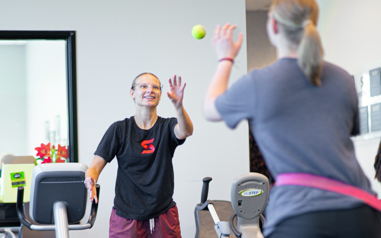 Molly Ahlemeier tossing a tennis ball to a teen athlete.