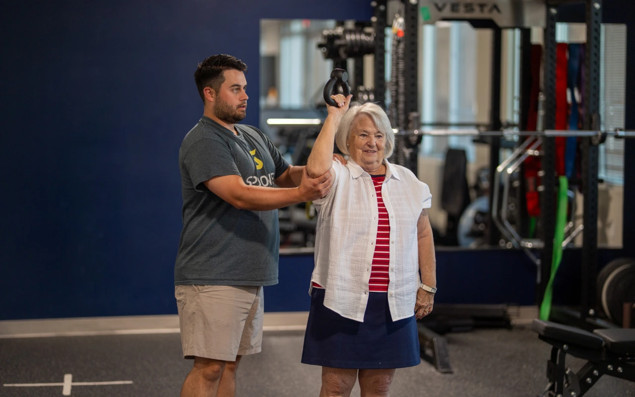 A physical therapist helping an older woman lift a kettlebell over her head