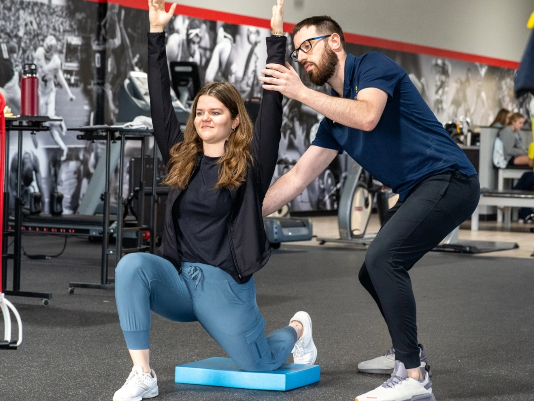 A physical therapist adjusts the position of a patient doing overhead raises.