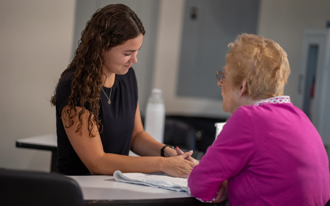A hand therapist working with an older woman in a pink shirt.