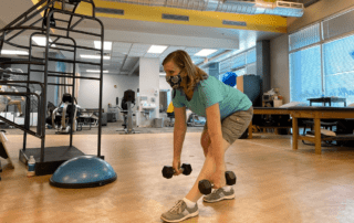 A woman holding dumbbells and leaning forward.