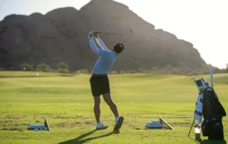 A golfer swinging on the turf towards a mountain.