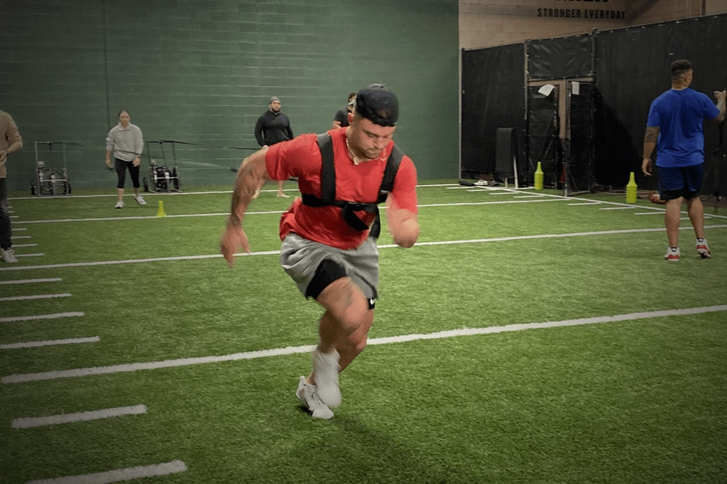 An athlete in a harness running while he pulls a sled.
