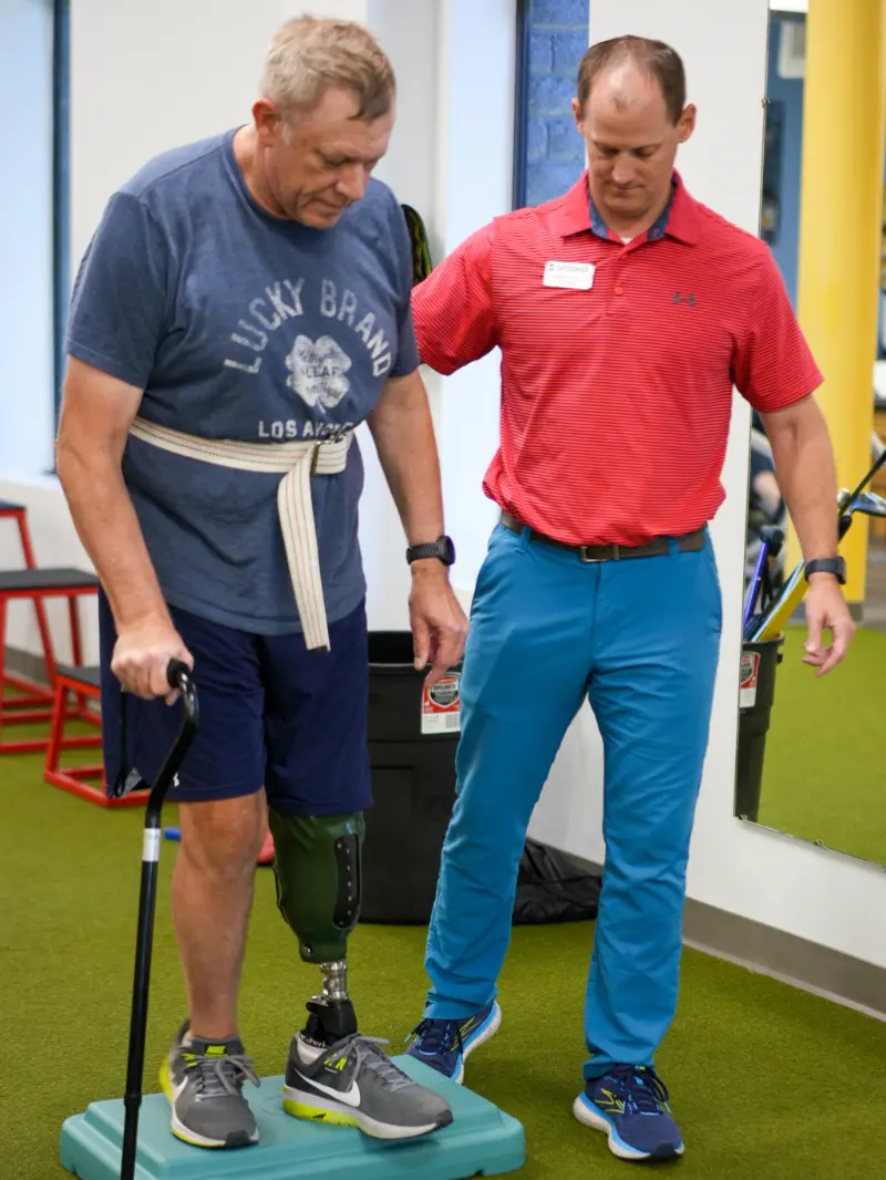 Amputee page image 1 Image of therapist helping a man with a prosthetic leg on a balance pad.