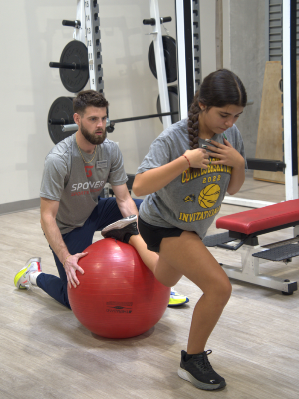 A physical therapists balancing a patient on a exercise ball.