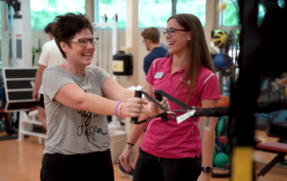 A woman pulls on a cable machine as her therapist watches.