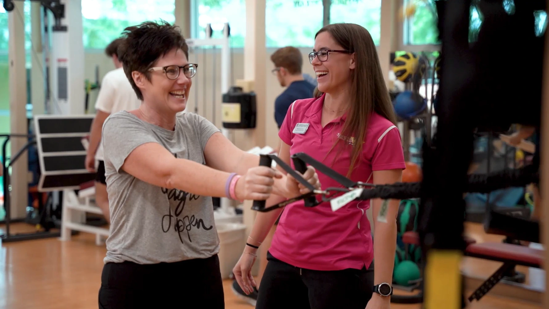 A woman pulls on a cable machine as her therapist watches.