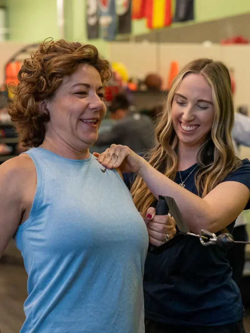 Image of a woman pulling on a cable machine with the assistance of a physical therapist.