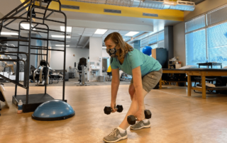 A woman holding dumbbells and leaning forward.
