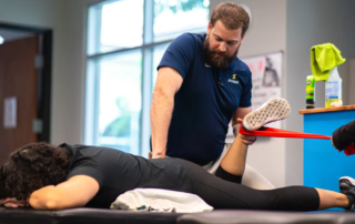 Nick Sutton, PT, DPT, CFMT treating a woman laying down on a table as she lifts her leg with a resistance band tied around it.