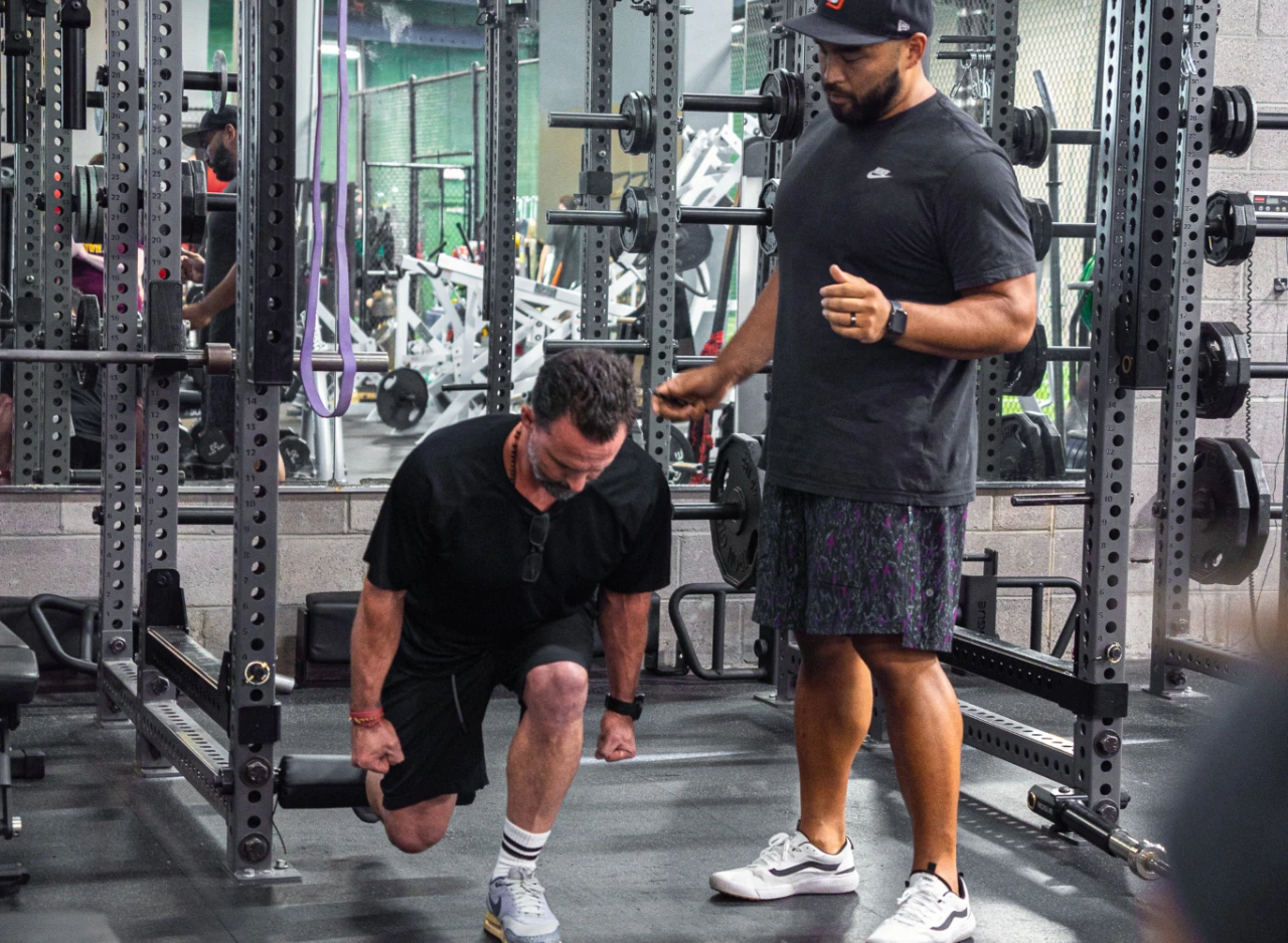 A man does a single leg lunge as a physical therapist monitors his movement.