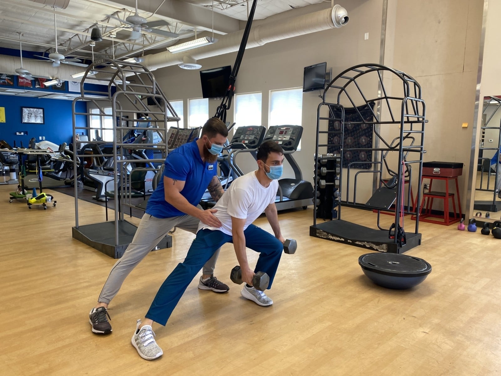 Man doing a sideways lunge as a FIT trainer supports him.