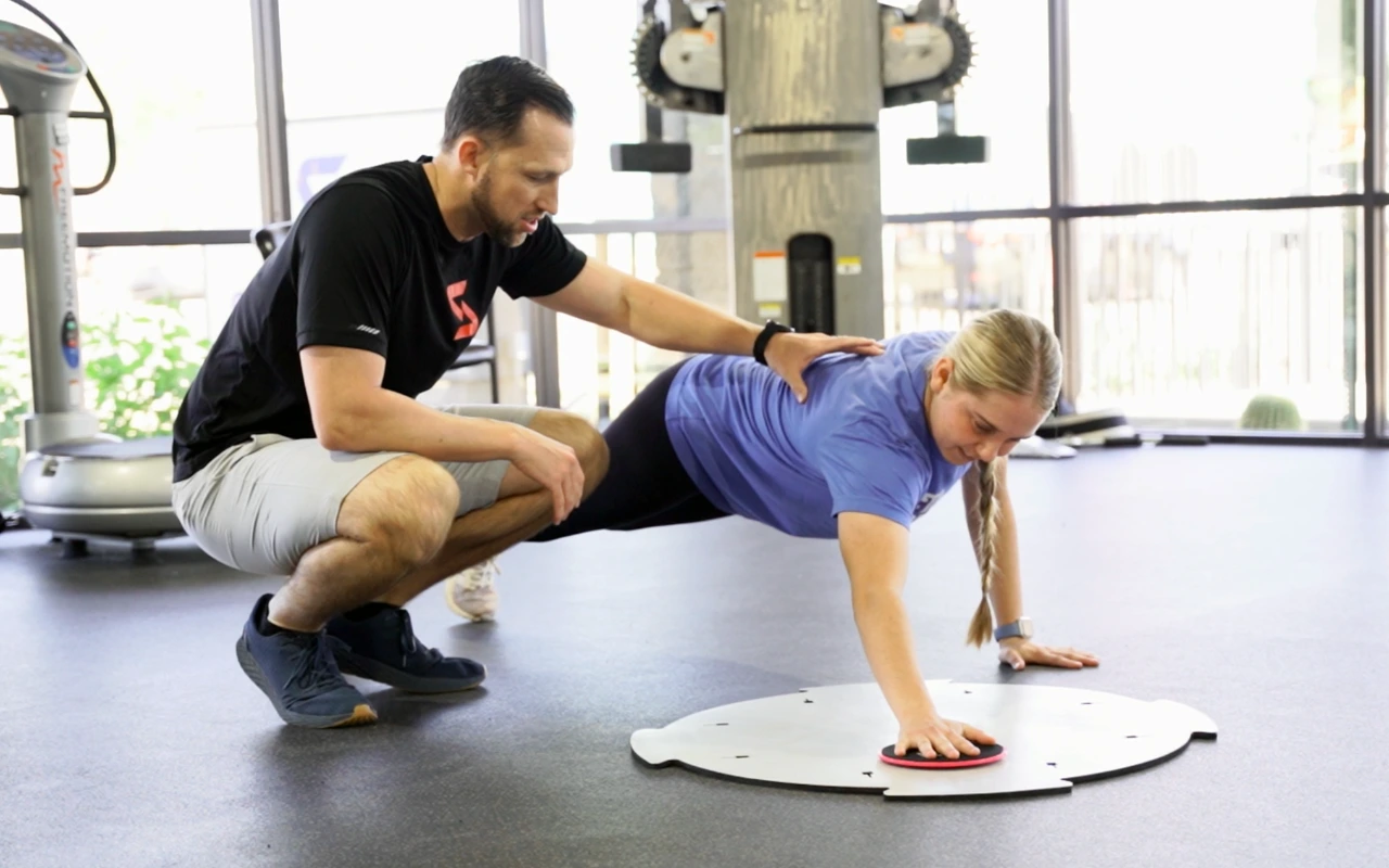 A woman doing a plank as a therapist stabilizes her.