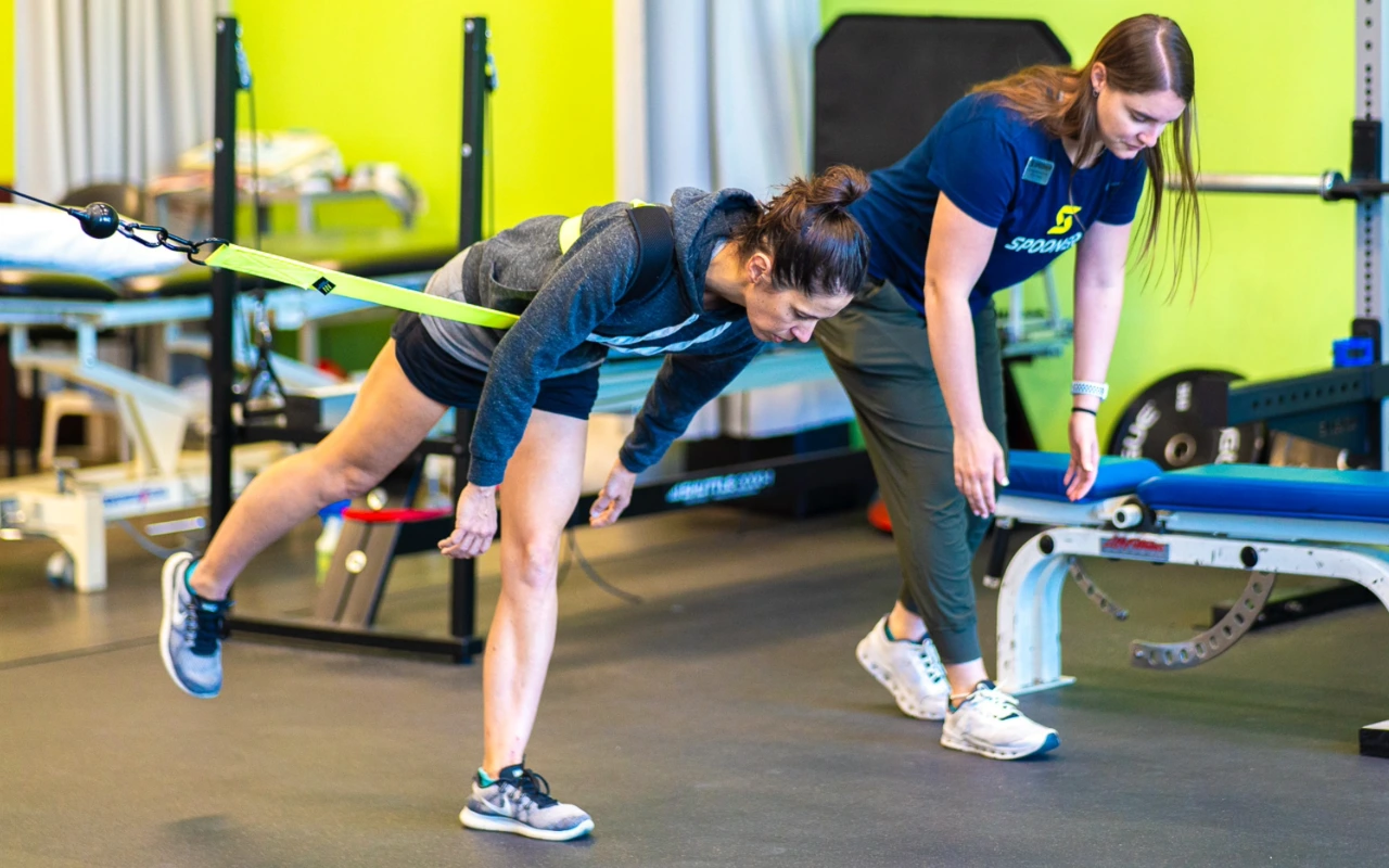 A woman stretching her hamstring with a resistance strap alongside a physical therapist.