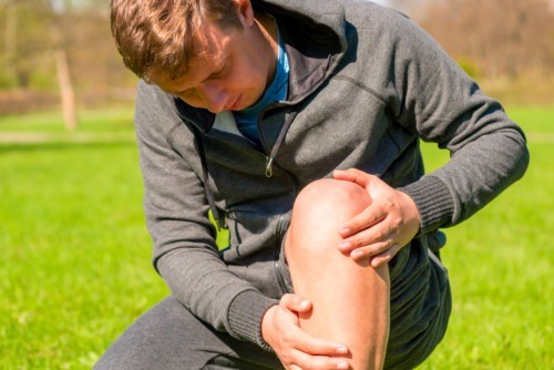 Man crouches down holding his knee