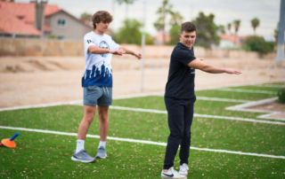 A lacrosse player trains with a physical therapist outside.