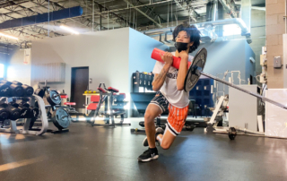 A young athlete lifting a barbell corner press at the Spooner Sports Institute.