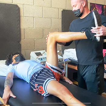 A young athlete laying on a table as he gets knee manipulation done for an injury.