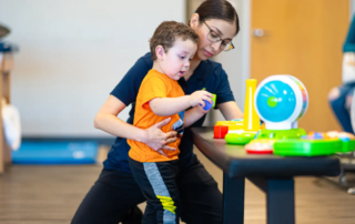 A toddler picking up blocks with a pediatric physical therapist.