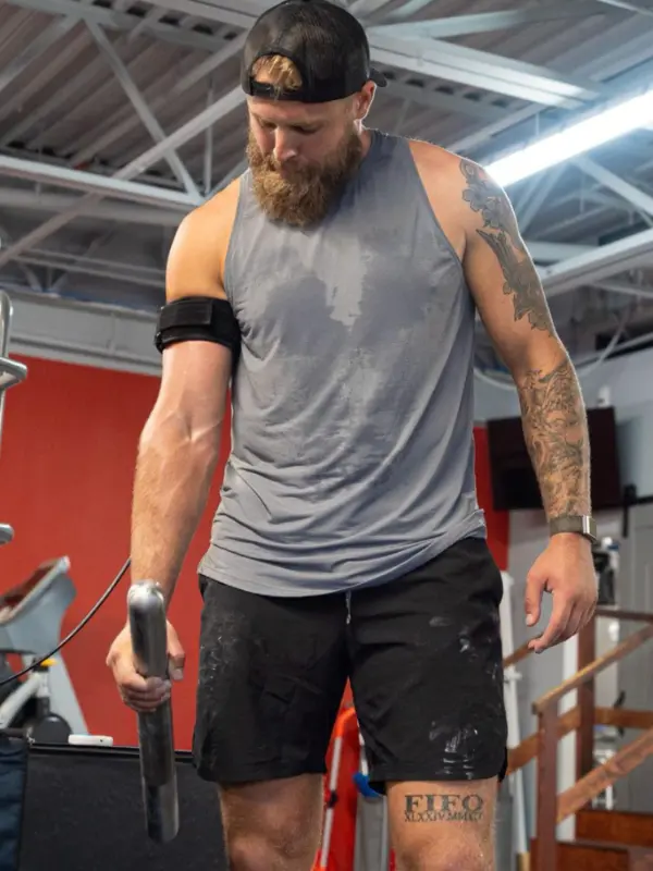 A male athlete with a Blood Flow Restriction (BFR) band on his arm as he exercises his arm with a weighted bar.