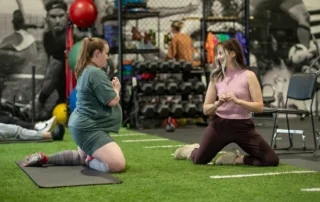 A pregnant woman doing pelvic floor exercises with her therapist on the ground.