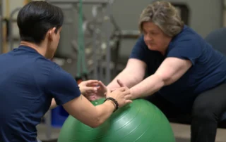 A woman does reaching exercises on an exercise ball while sitting down at the Spooner Peoria clinic.