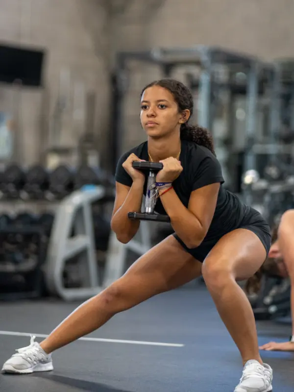 A female youth athlete does a sideways lunge while holding a dumbbell.