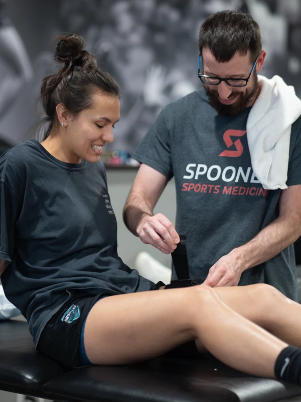 Rockwall Sports Med A sports medicine therapist tying a strap to a woman's leg.