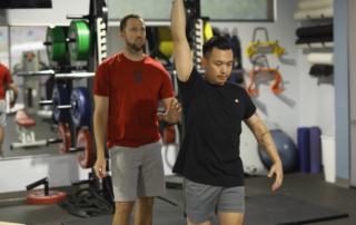 Dillon Moeller, PT, DPT watching a patient as they lift a kettlebell overhead.