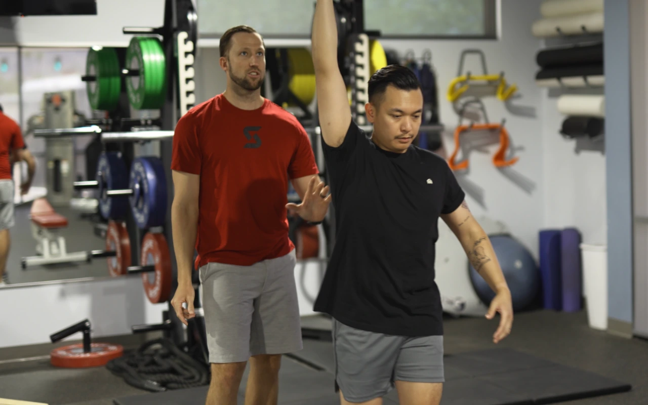 Dillon Moeller, PT, DPT watching a patient as they lift a kettlebell overhead.